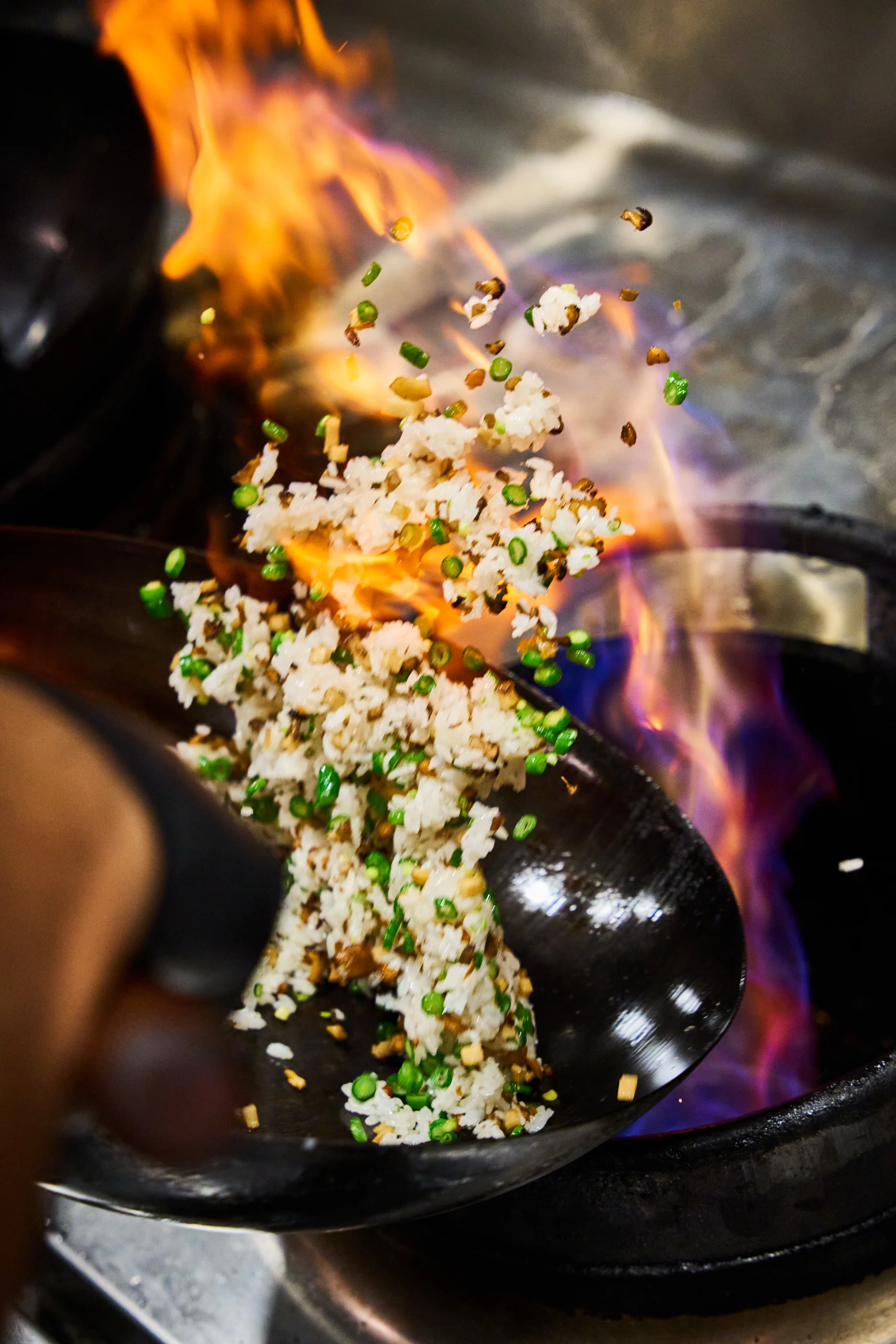 A chef tossing fried rice over a roaring wok flame