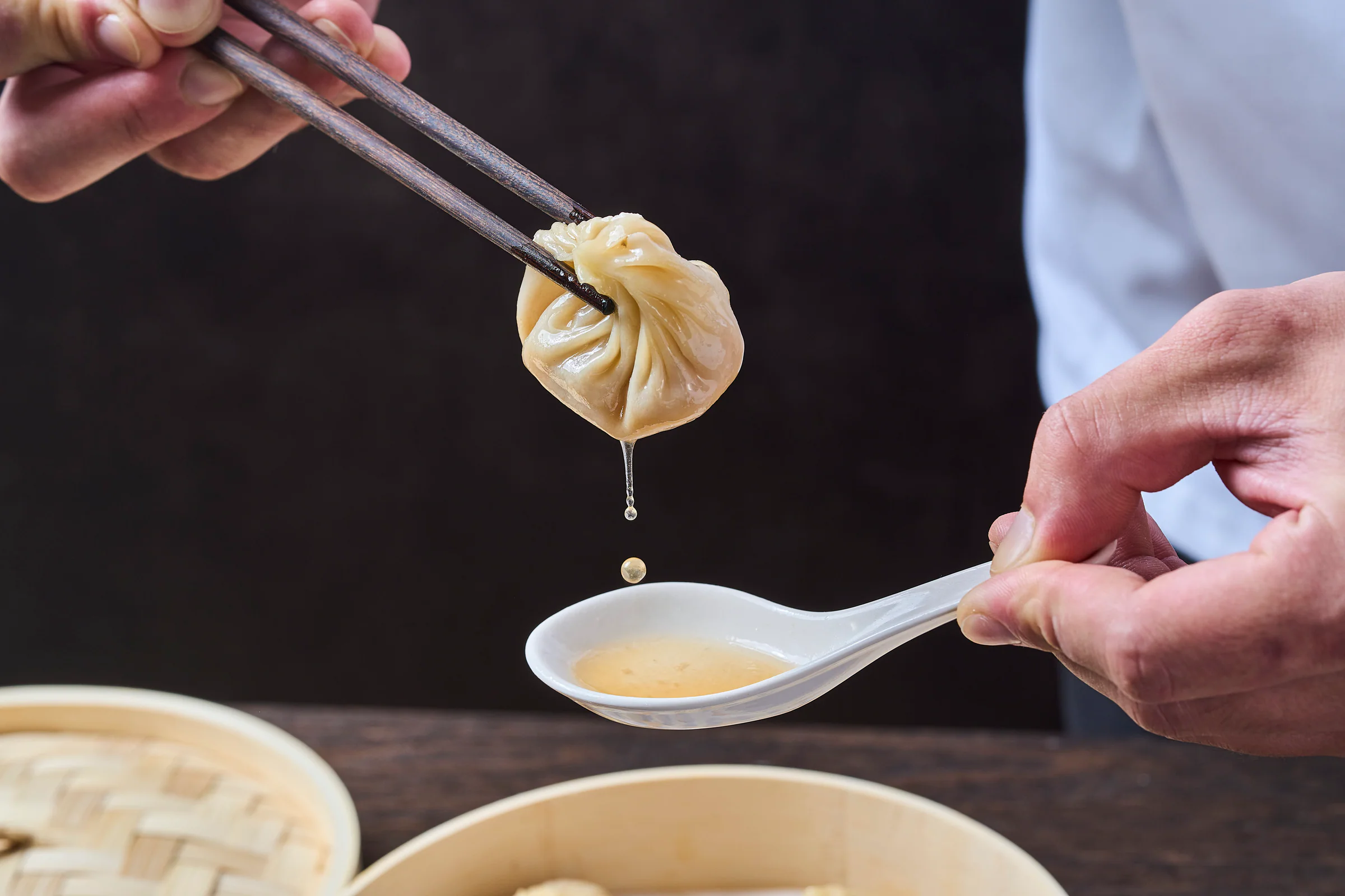 Broth dripping from a freshly lifted Xiao Long Bao into a soup spoon
