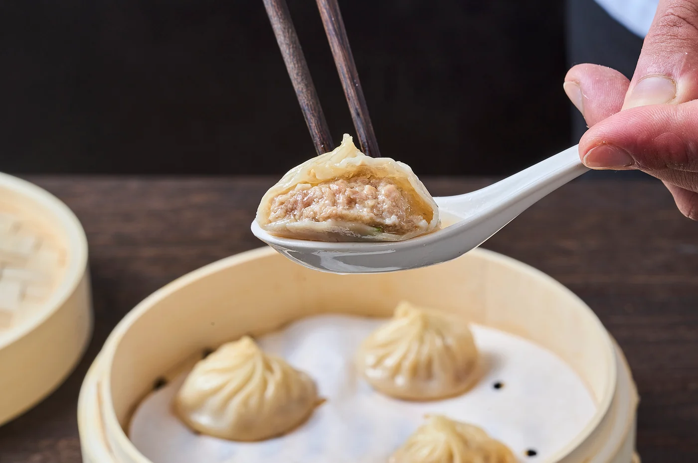 A juicy Xiao Long Bao opened over a spoon, ready for a perfect bite