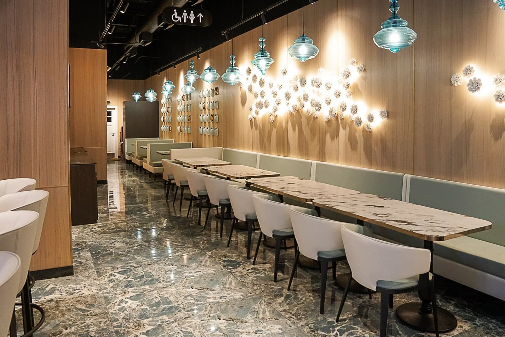 The Bellevue dining room: banquettes and marble tables along a wood-paneled wall hung with teal glass pendants