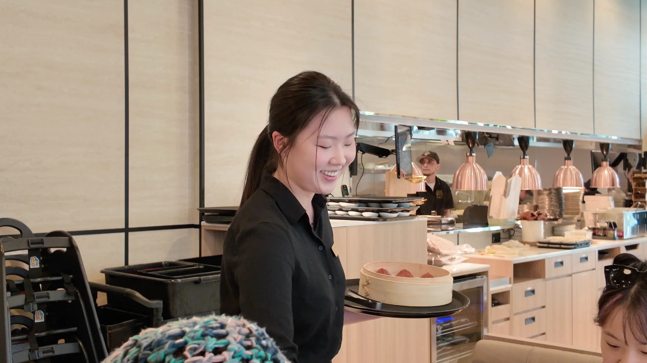 A smiling Supreme Dumplings server bringing a bamboo steamer to guests